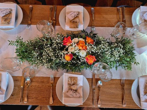 Tisch mit weißem Tuch, Blumenarrangement und gedecktem Geschirr.