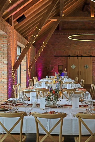 Elegant gedeckter Tisch in einem festlichen Saal mit Holzbalkendecke und bunten Lichtern.