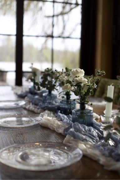 Tischgedeck mit floraler Dekoration und leichten Textilien in einem hellen Raum.