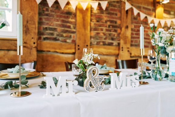 Tischdeko mit „Mr & Mrs“-Schildern, Blumen und Kerzen in rustikalem Ambiente.