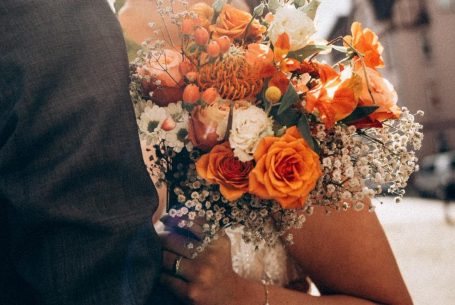 Hochzeitsstrauß mit orangefarbenen Rosen und bunten Blumen im Sonnenlicht.