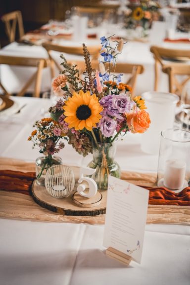 Vase mit Sonnenblumen und bunten Blumenarrangements auf einem Tisch.