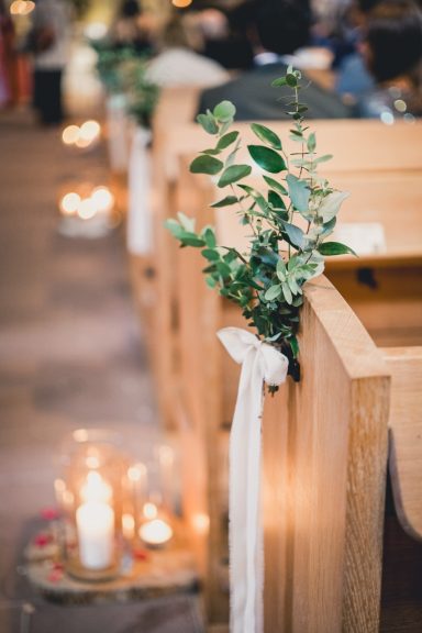 Bänke mit grüner Dekoration und Kerzen in einer festlichen Umgebung.