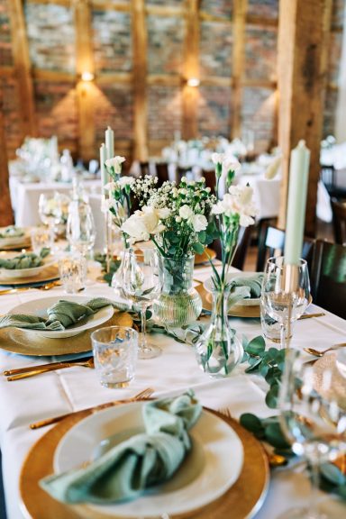 Elegant gedeckte Tafel mit Blumen, Kerzen und grün-goldenem Dekor.